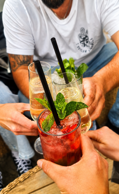 Verschiedene Cocktails mit Minze werden von mehreren Personen gehalten. Mojito, Erdbeer-Mojito, Sekt