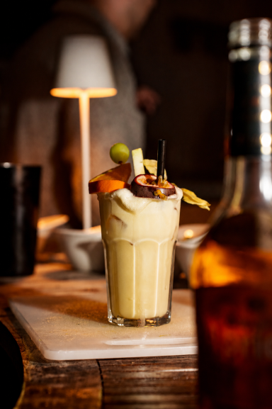 Ein dekorierter Cocktail mit Sahne, Früchten und einem bunten Schirmchen in einem Glas. Passionfruit ala Ray
