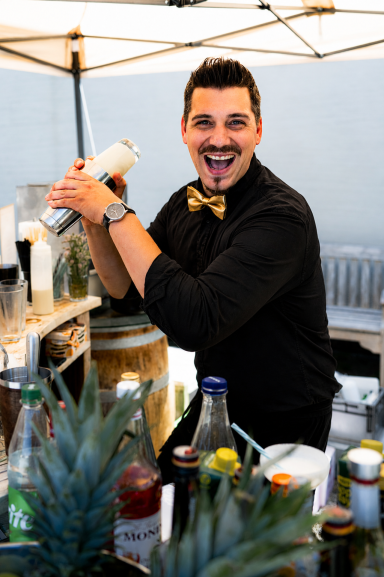 Bartender mixt Cocktails hinter einer Bar, umgeben von Flaschen und Ananas. Pina Colada